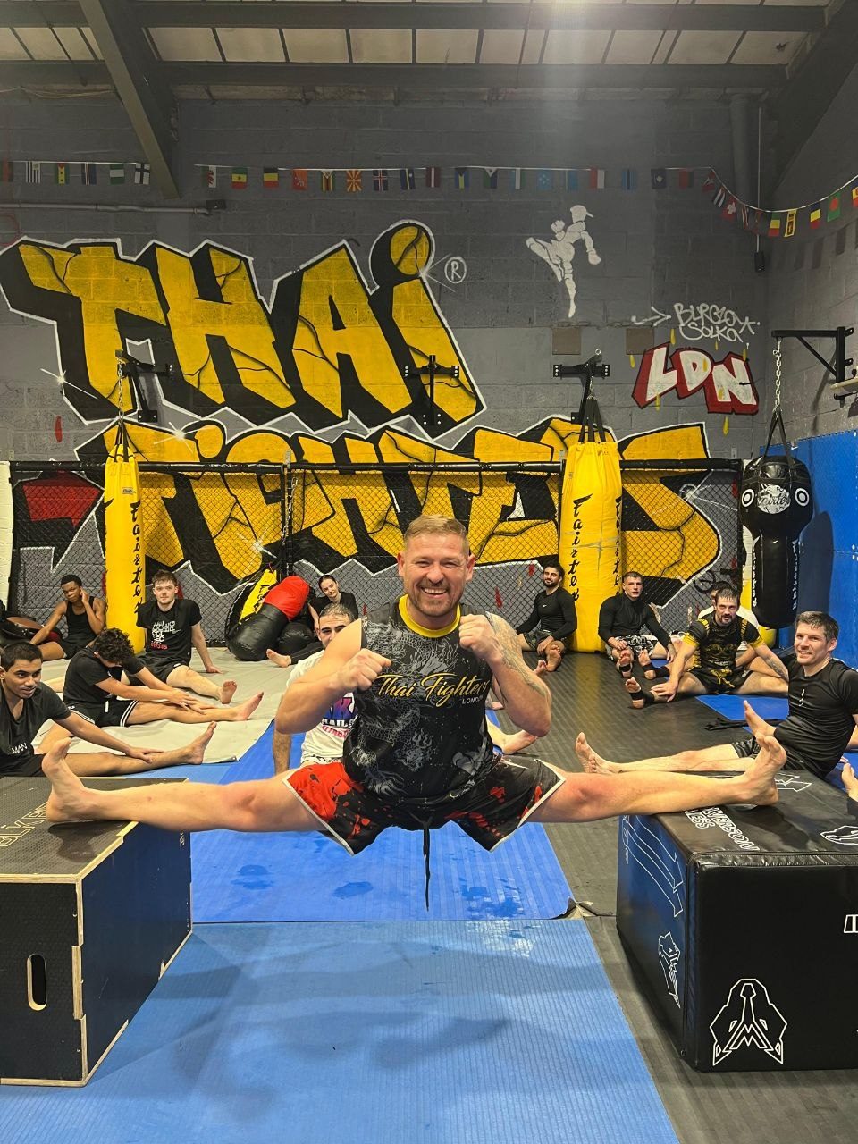 Darius Skliaudys holding a mid-air split in front of the Thai Fighters wall while his class stretches behind him